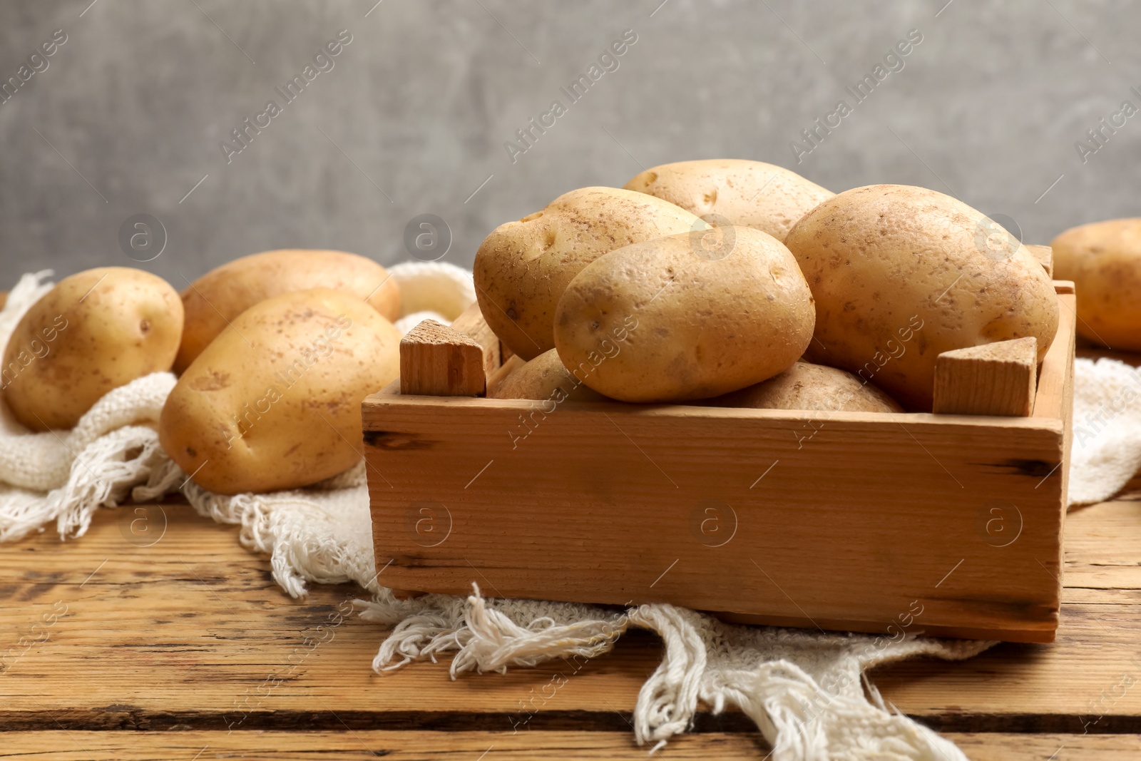 Photo of Many fresh potatoes in crate on wooden table, closeup