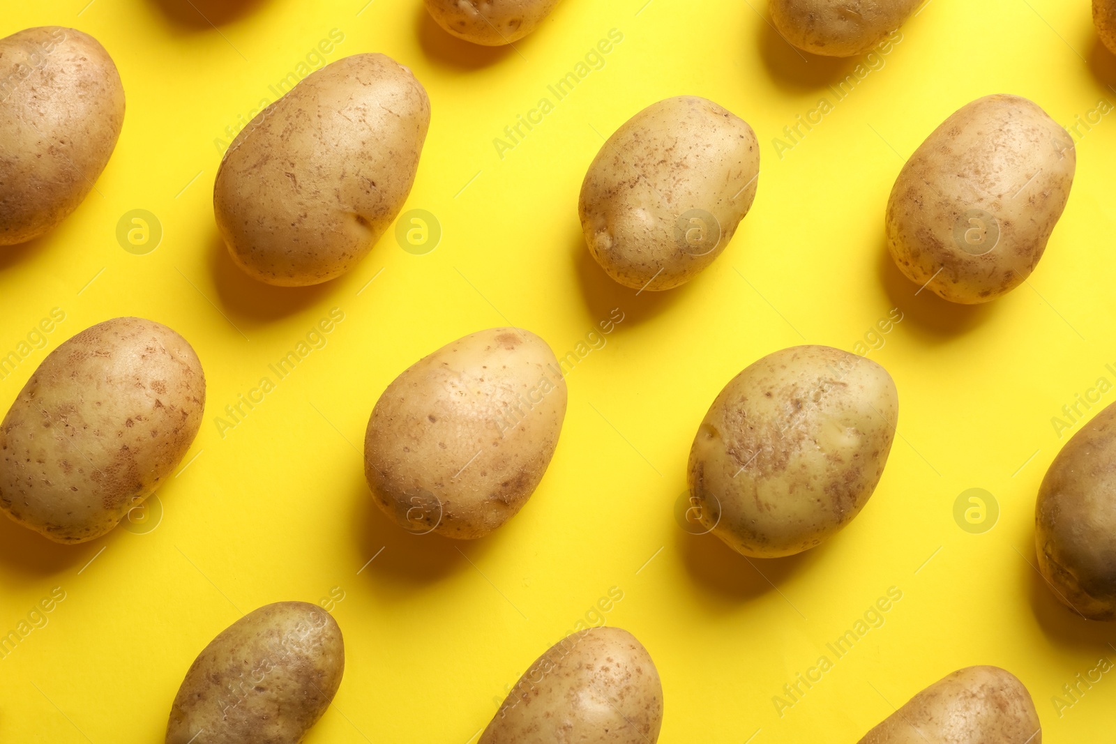 Photo of Many fresh potatoes on yellow background, flat lay