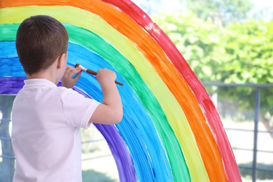 Little boy drawing rainbow on window indoors, back view