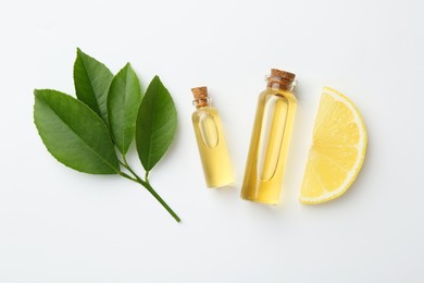 Bottles of essential oils, lemon and green leaves on white background, flat lay