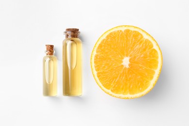 Bottles of essential oils and orange on white background, flat lay