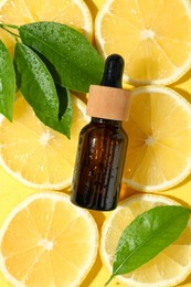 Photo of Bottle of essential oil, lemon and green leaves on yellow background, flat lay