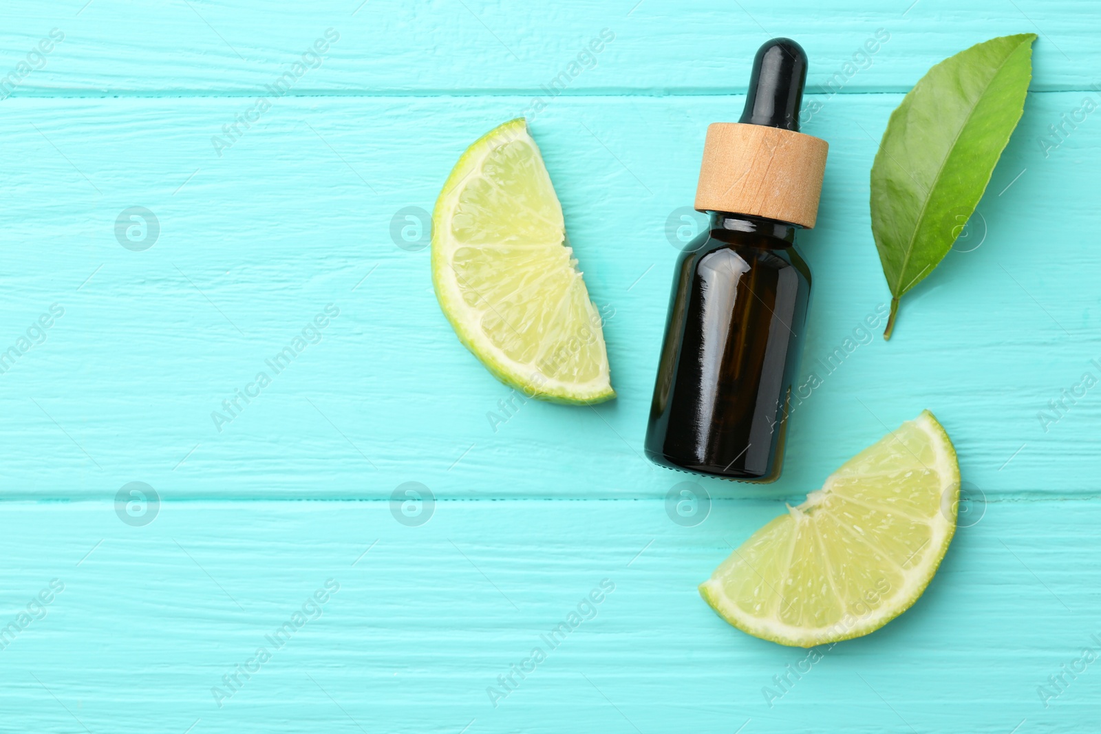 Photo of Bottle of essential oil, lime and green leaf on turquoise wooden table, flat lay. Space for text