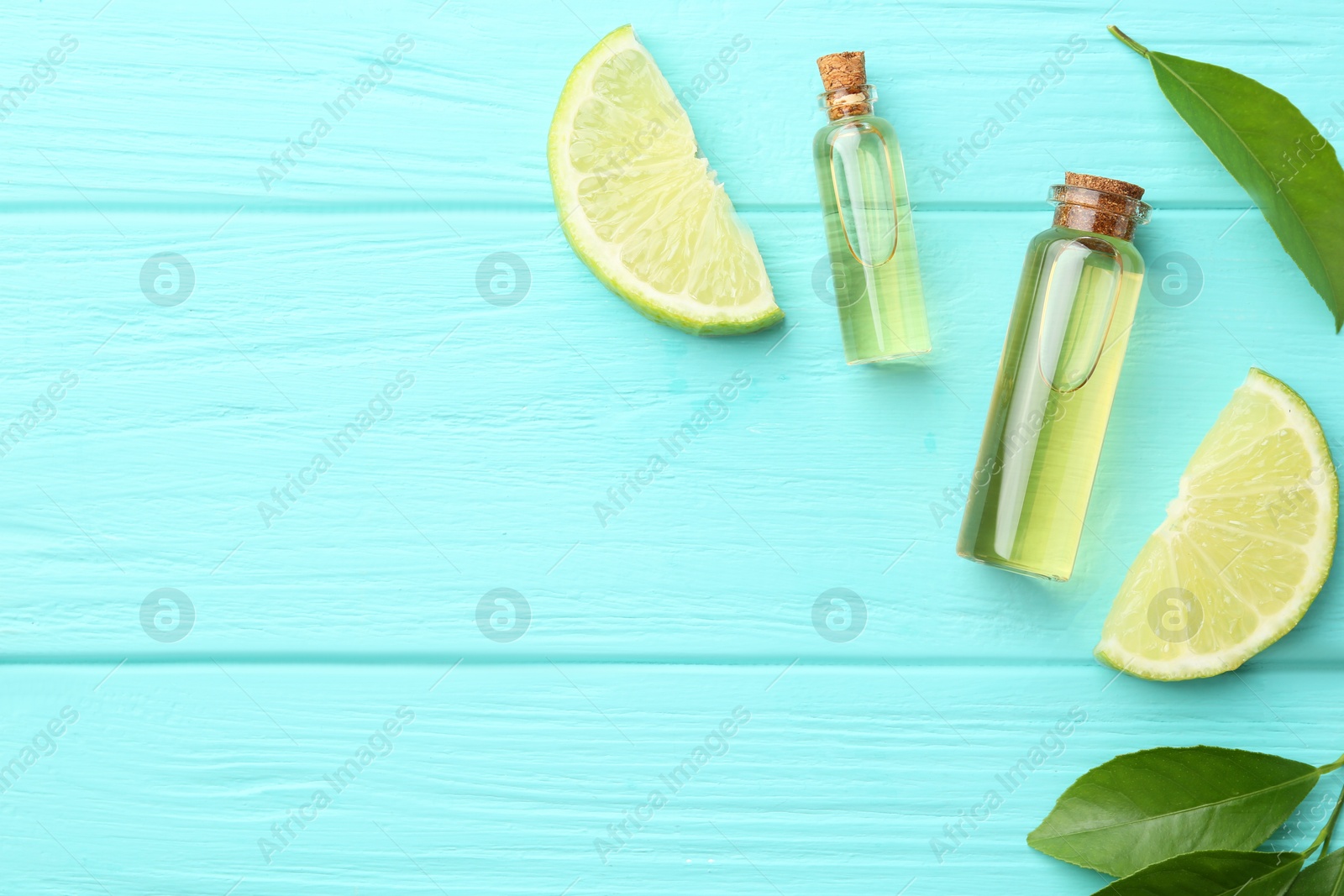 Photo of Bottles of essential oils, lime and green leaves on turquoise wooden table, flat lay. Space for text