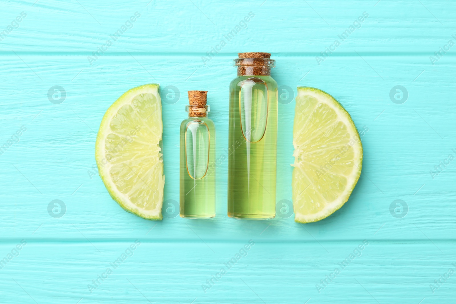 Photo of Bottles of essential oils and lime on turquoise wooden table, flat lay