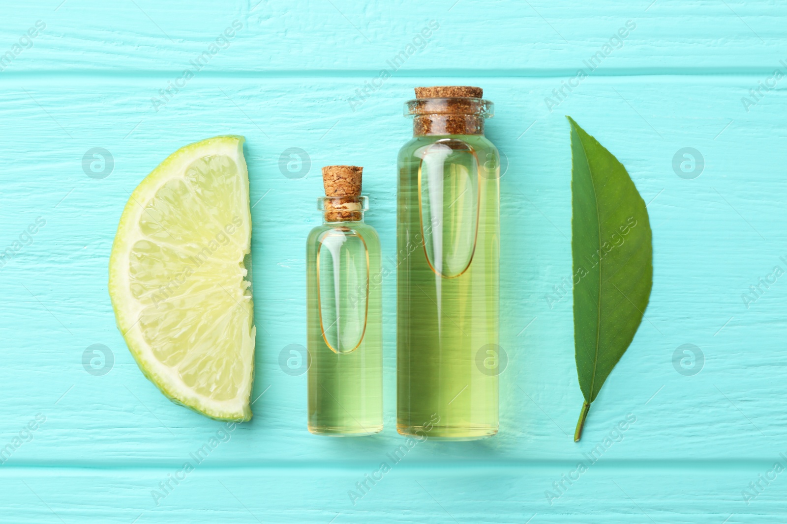 Photo of Bottles of essential oils, lime and green leaf on turquoise wooden table, flat lay