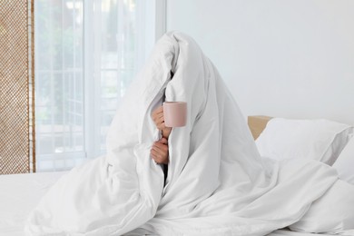 Bedtime. Woman wrapped in blanket holding cup of drink on bed indoors