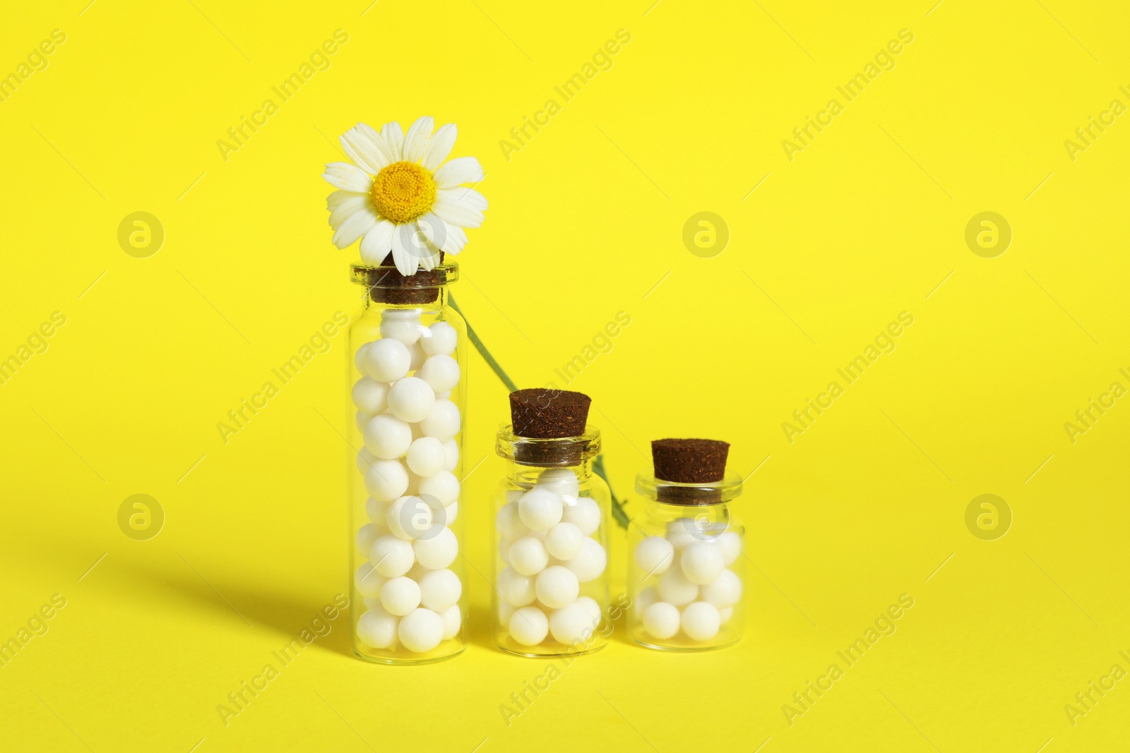 Photo of Bottles with homeopathic remedy and chamomile on yellow background