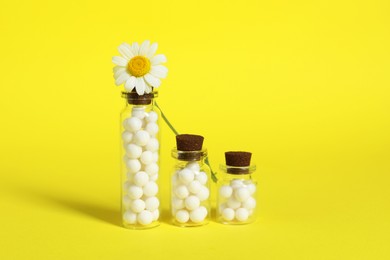 Photo of Bottles with homeopathic remedy and chamomile on yellow background