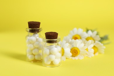 Bottles with homeopathic remedy and chamomiles on yellow background, selective focus