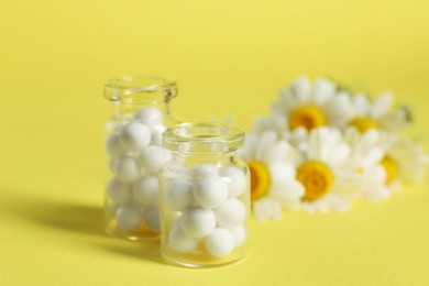 Bottles with homeopathic remedy and chamomiles on yellow background, selective focus