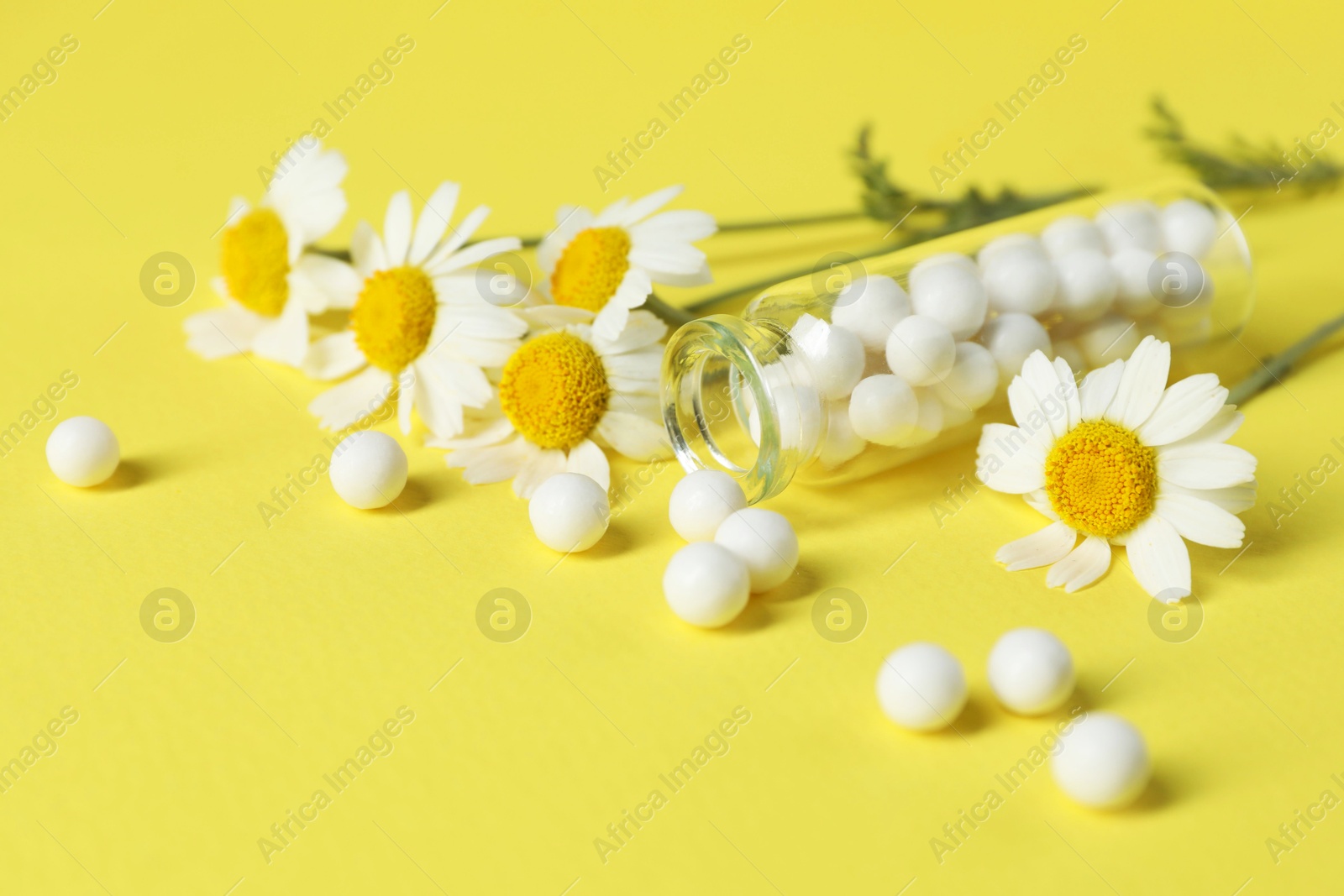 Photo of Bottle with homeopathic remedy and chamomiles on yellow background, closeup