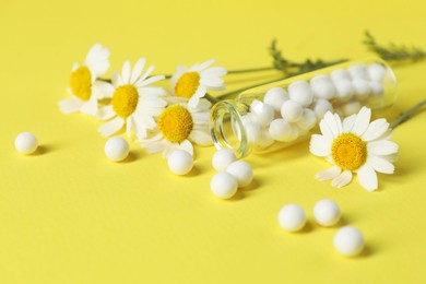 Bottle with homeopathic remedy and chamomiles on yellow background, closeup