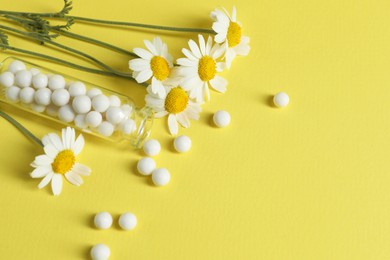 Photo of Bottle with homeopathic remedy and chamomiles on yellow background. Space for text