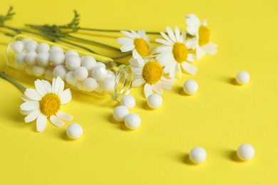 Photo of Bottle with homeopathic remedy and chamomiles on yellow background, closeup