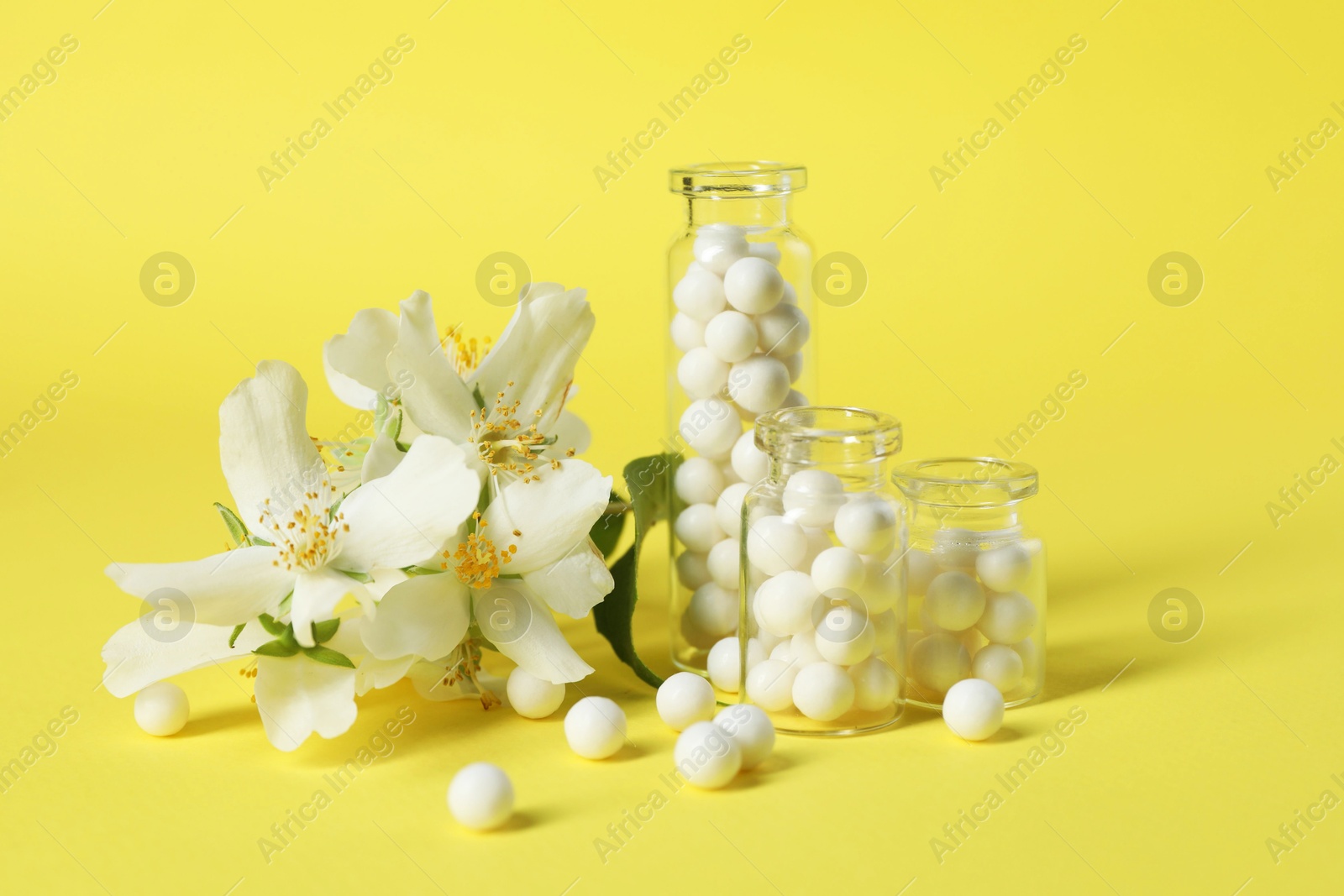 Photo of Bottles with homeopathic remedy and flowers on yellow background