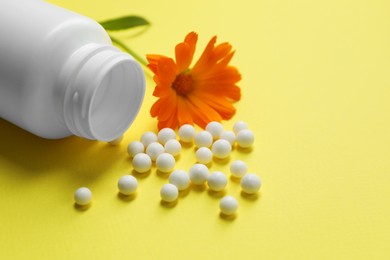 Homeopathic remedy, bottle and calendula on yellow background, closeup. Space for text