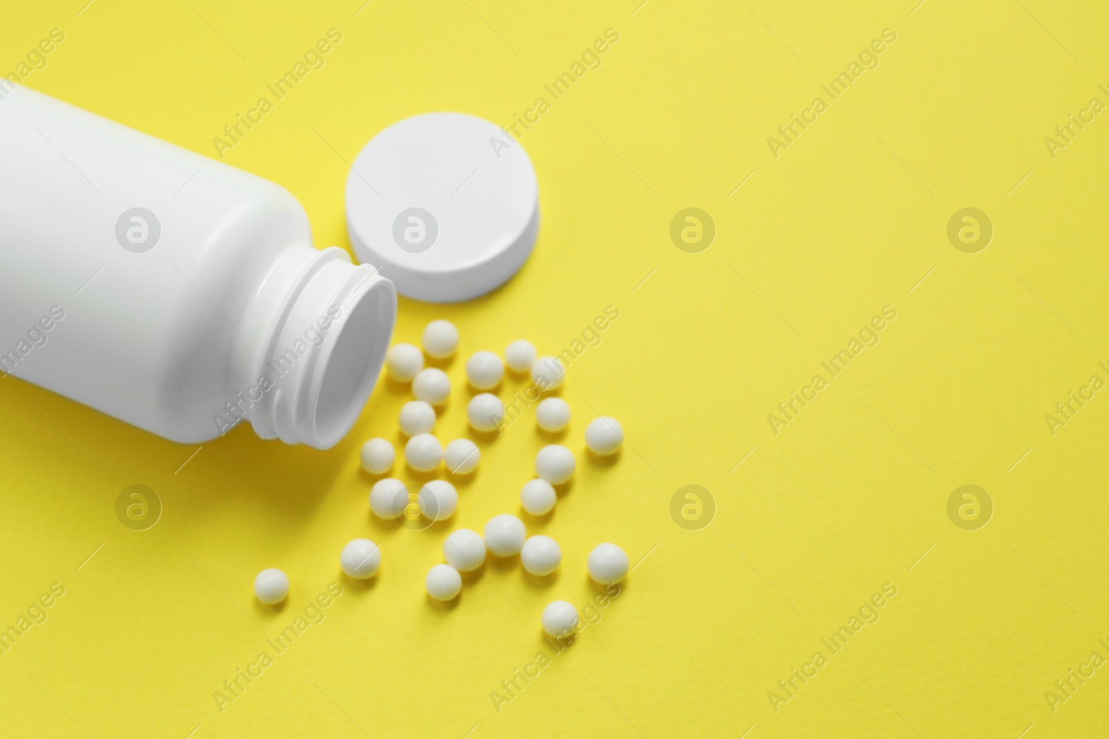 Photo of Homeopathic remedy and bottle on yellow background. Space for text