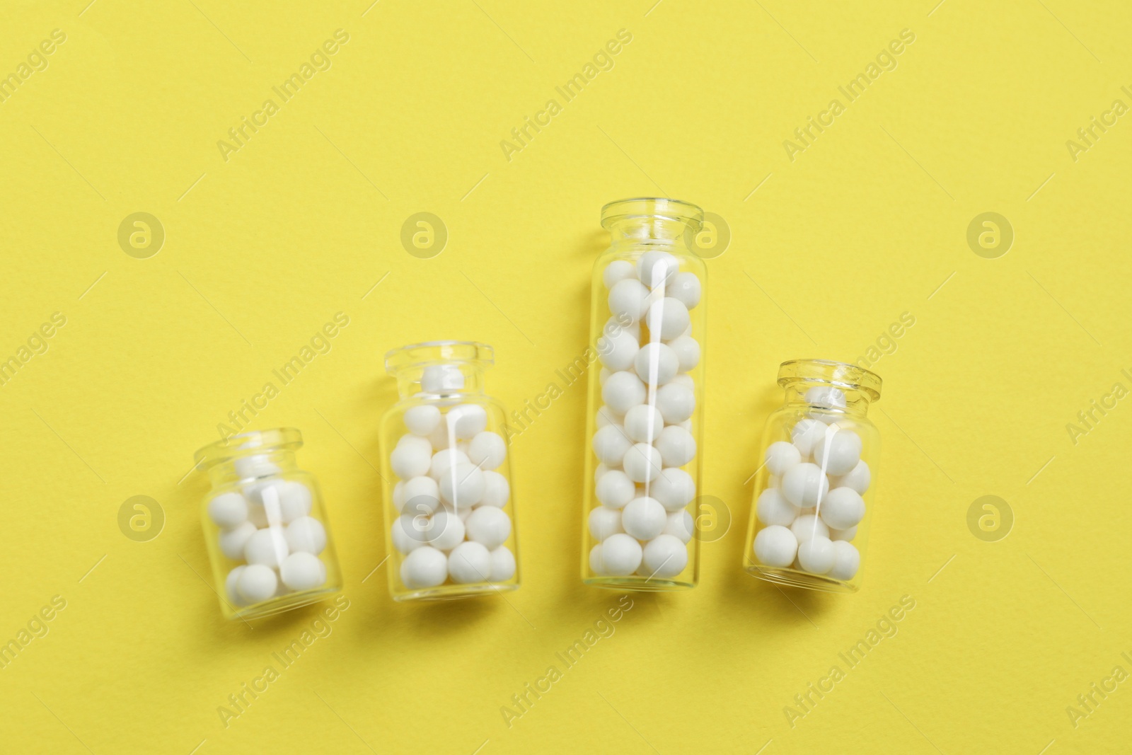 Photo of Bottles with homeopathic remedy on yellow background, flat lay