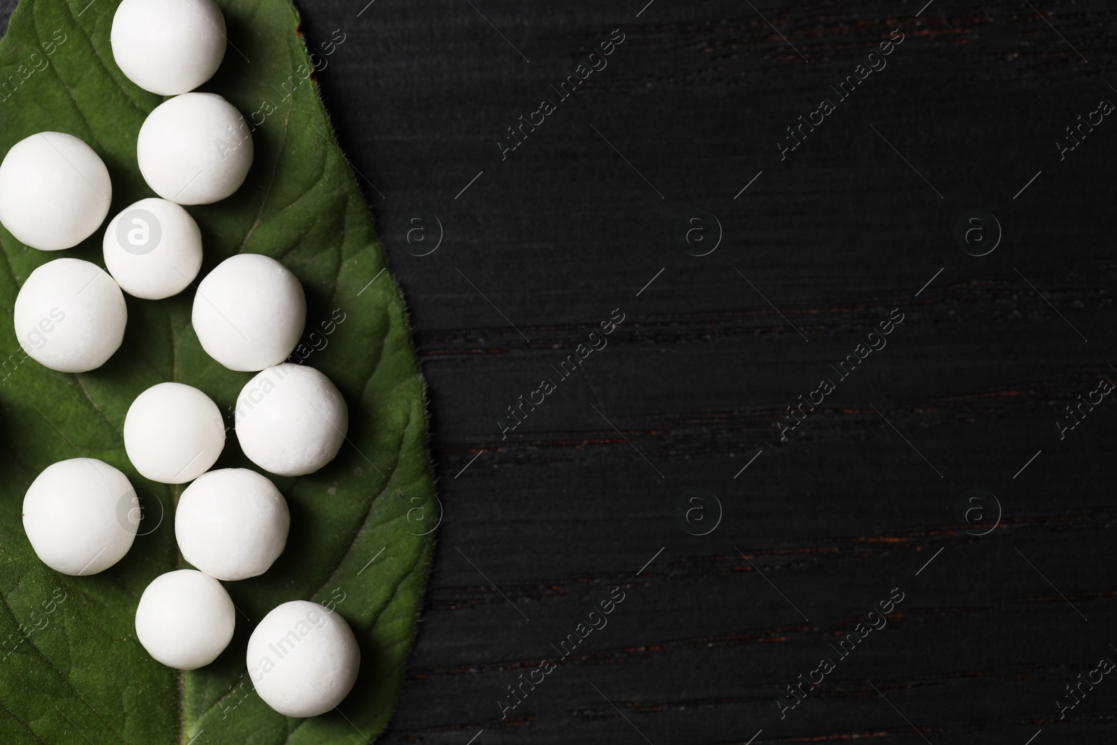 Photo of Homeopathy. Many pills and green leaf on black wooden table, top view. Space for text