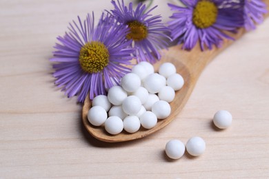 Photo of Homeopathy. Spoon with pills and wild flowers on wooden table, closeup