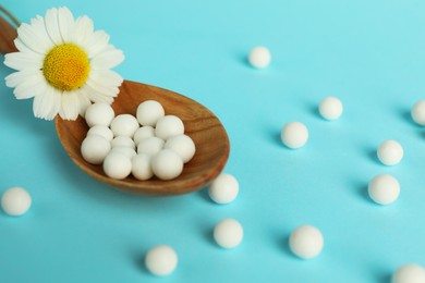 Photo of Homeopathy. Spoon with many pills and chamomile flower on light blue background