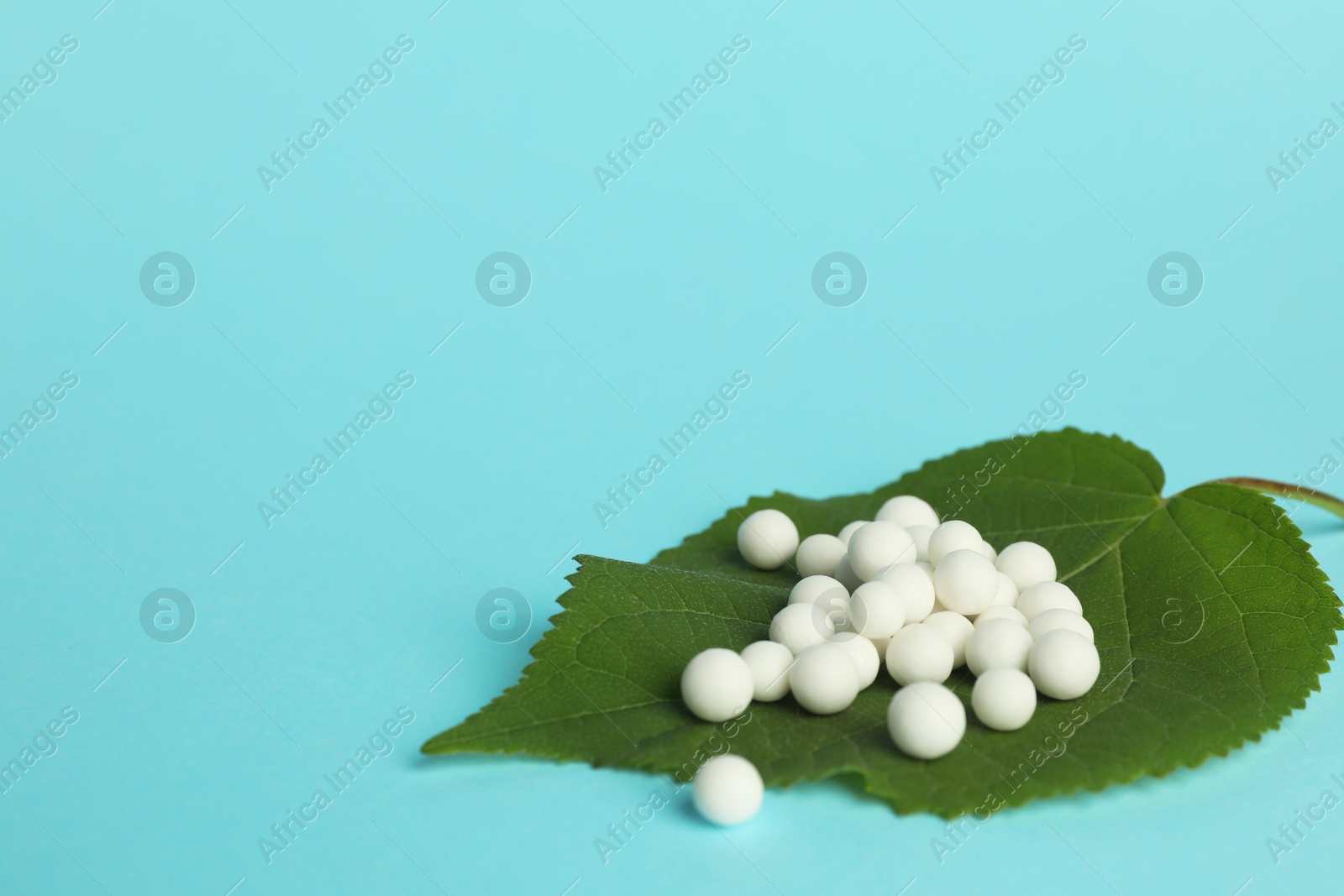 Photo of Homeopathy. Many pills and green leaf on light blue background, space for text