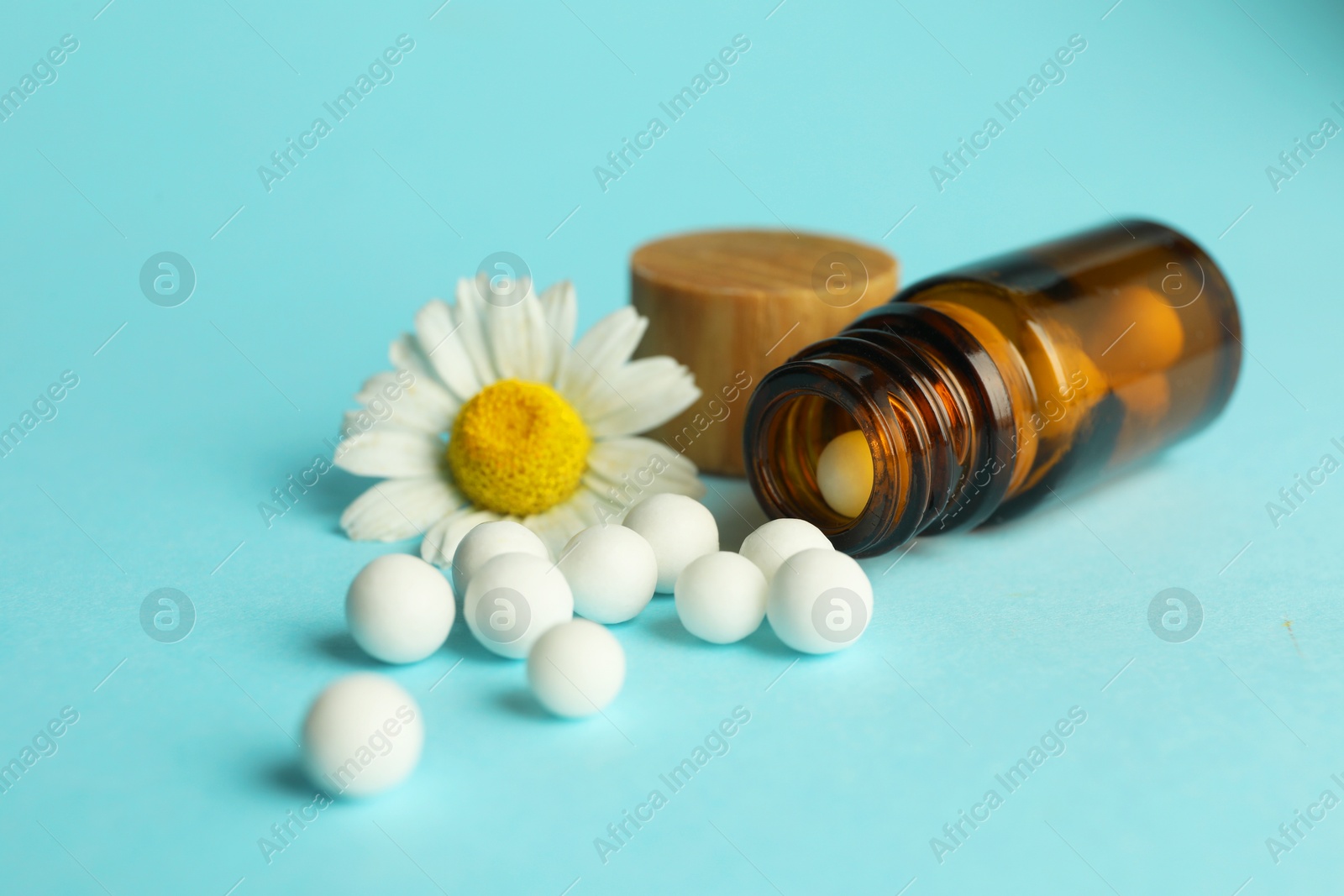 Photo of Homeopathy. Bottle with pills and chamomile flower on light blue background, closeup