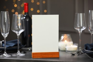 Photo of Menu holder, clean dishware and burning candles on gray table against blurred lights