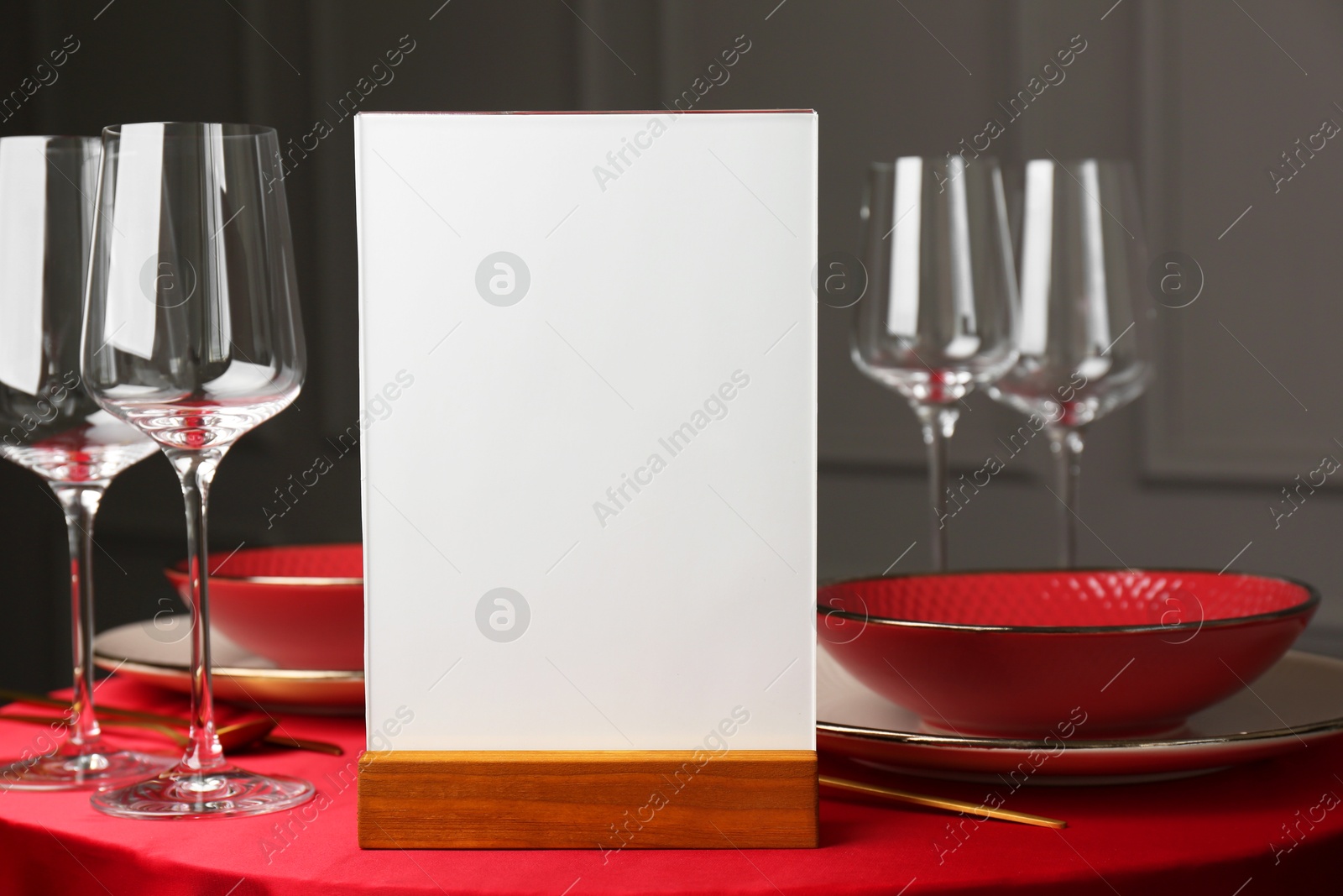 Photo of Menu holder, clean dishware and cutlery on red table in restaurant