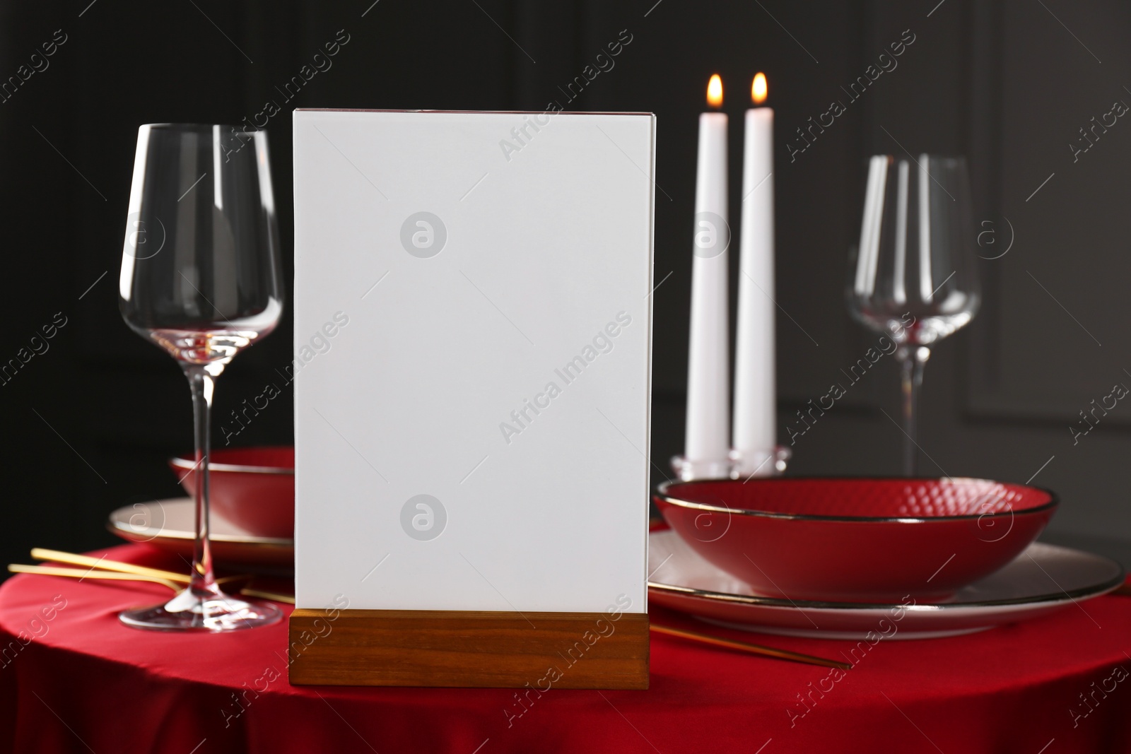 Photo of Menu holder, clean dishware and cutlery on red table in restaurant