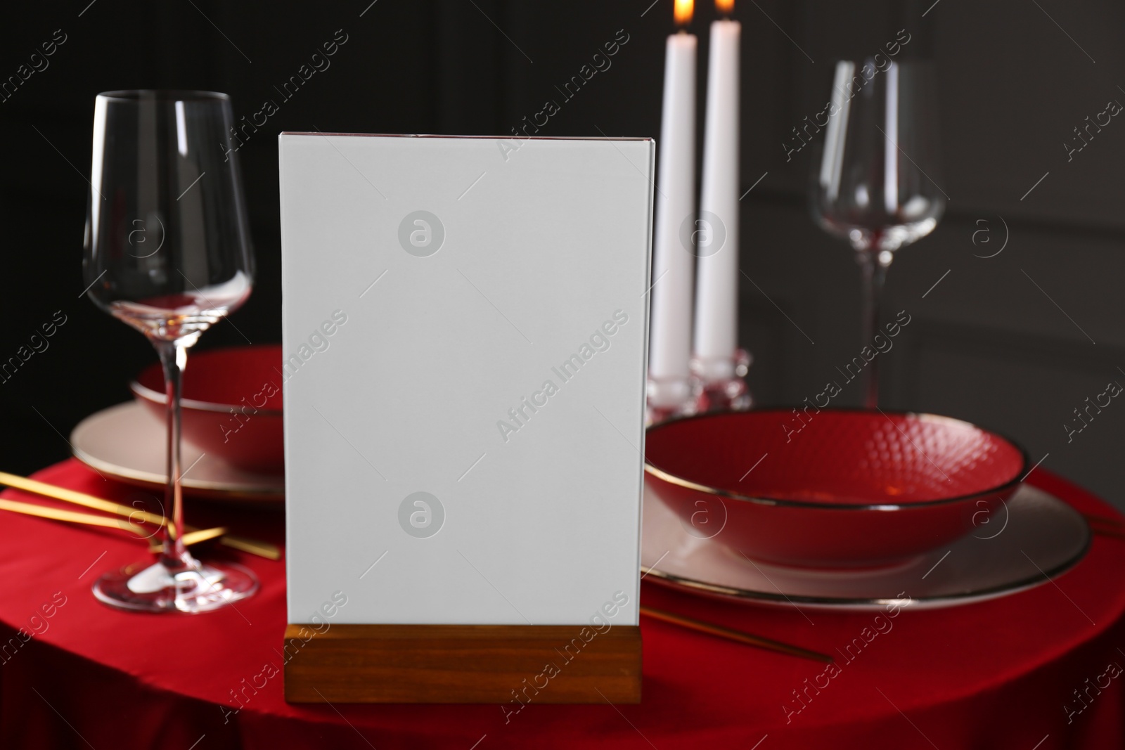 Photo of Menu holder, clean dishware and cutlery on red table in restaurant, closeup