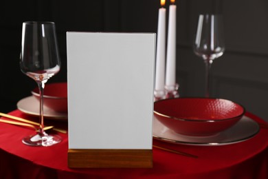 Photo of Menu holder, clean dishware and cutlery on red table in restaurant, closeup