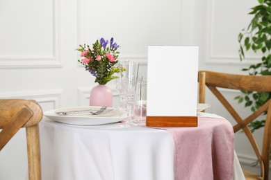 Photo of Menu holder, clean dishware and vase with beautiful flowers on white table in restaurant