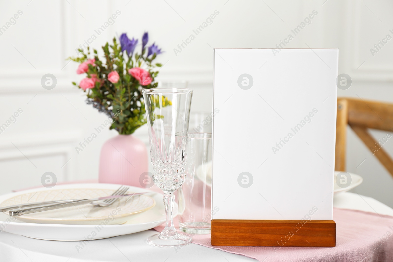 Photo of Menu holder, clean dishware and vase with beautiful flowers on white table in restaurant