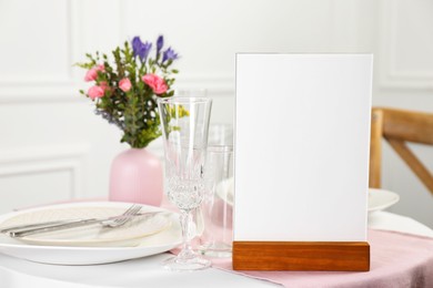 Photo of Menu holder, clean dishware and vase with beautiful flowers on white table in restaurant