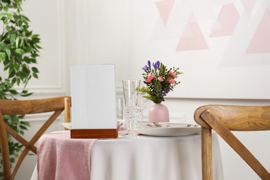 Photo of Menu holder, clean dishware and vase with beautiful flowers on white table in restaurant