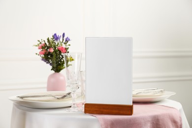 Photo of Menu holder, clean dishware and vase with beautiful flowers on white table in restaurant