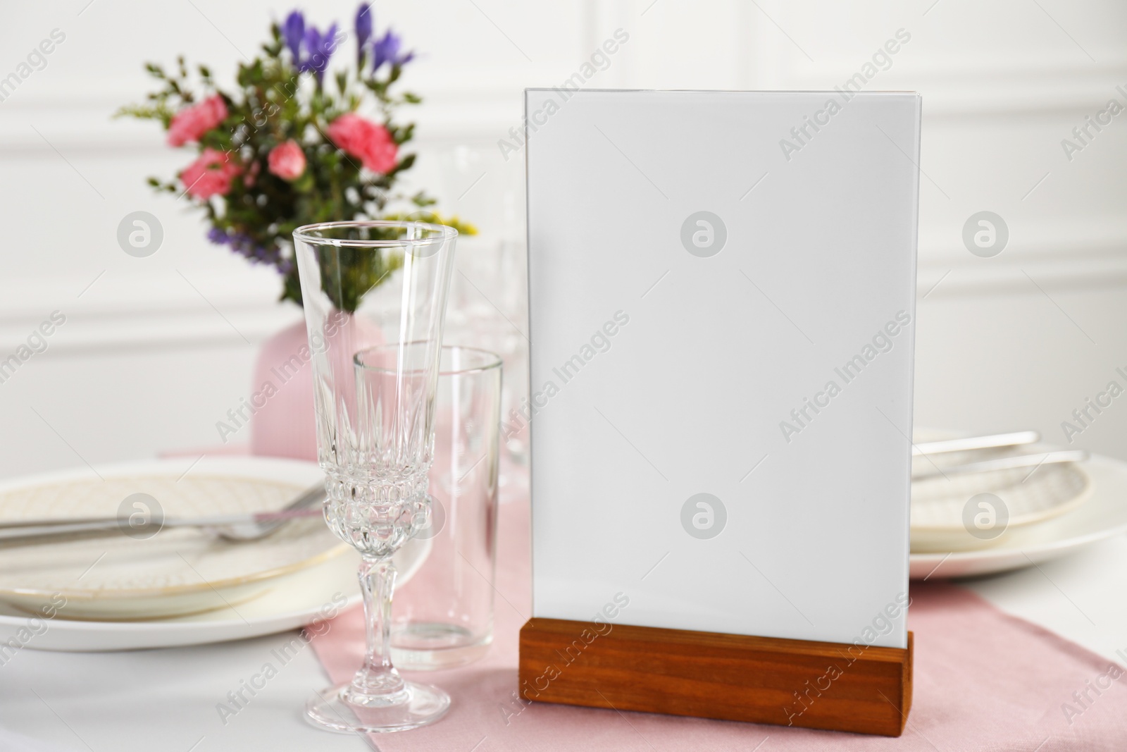 Photo of Menu holder, clean dishware and vase with beautiful flowers on white table in restaurant, closeup