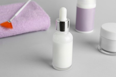 Photo of Bottle of chemical peel, cosmetic products, towel and brush on light background, closeup. Peeling procedure