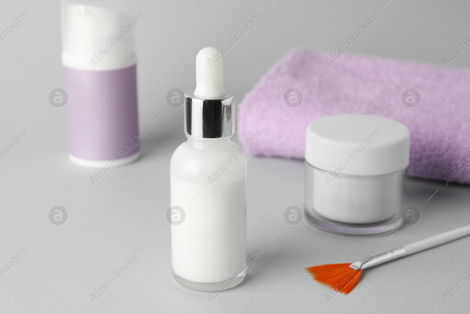 Photo of Bottle of chemical peel, cosmetic products, towel and brush on light background, closeup. Peeling procedure