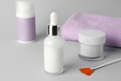 Photo of Bottle of chemical peel, cosmetic products, towel and brush on light background, closeup. Peeling procedure