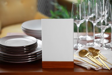 Photo of Menu holder, clean dishware and cutlery on wooden table indoors