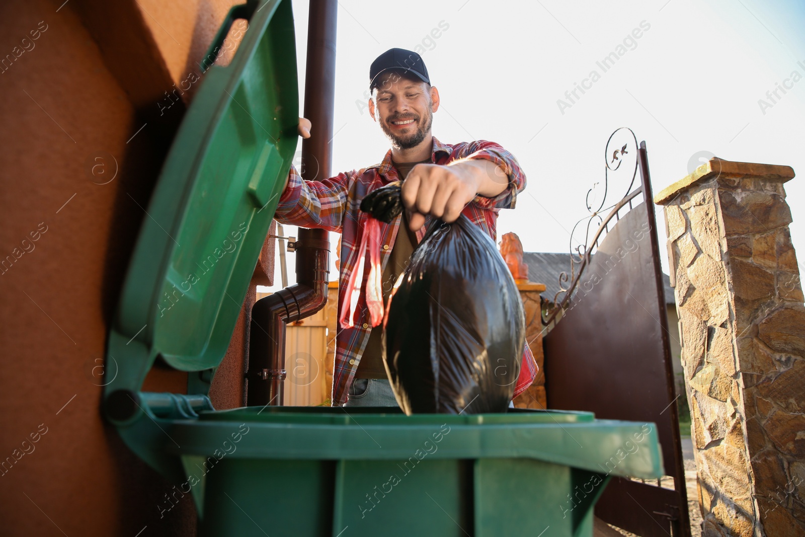 Photo of Man throwing trash bag full of garbage into bin outdoors, low angle view