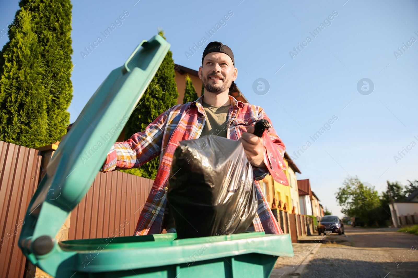 Photo of Man throwing trash bag full of garbage into bin outdoors, low angle view. Space for text