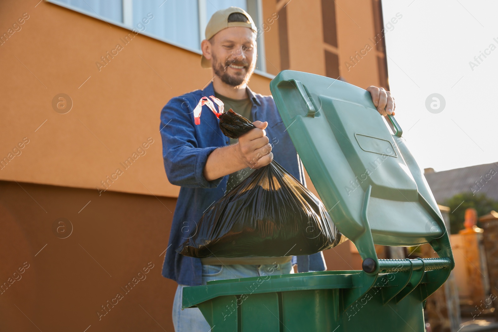 Photo of Man throwing trash bag full of garbage into bin outdoors, space for text