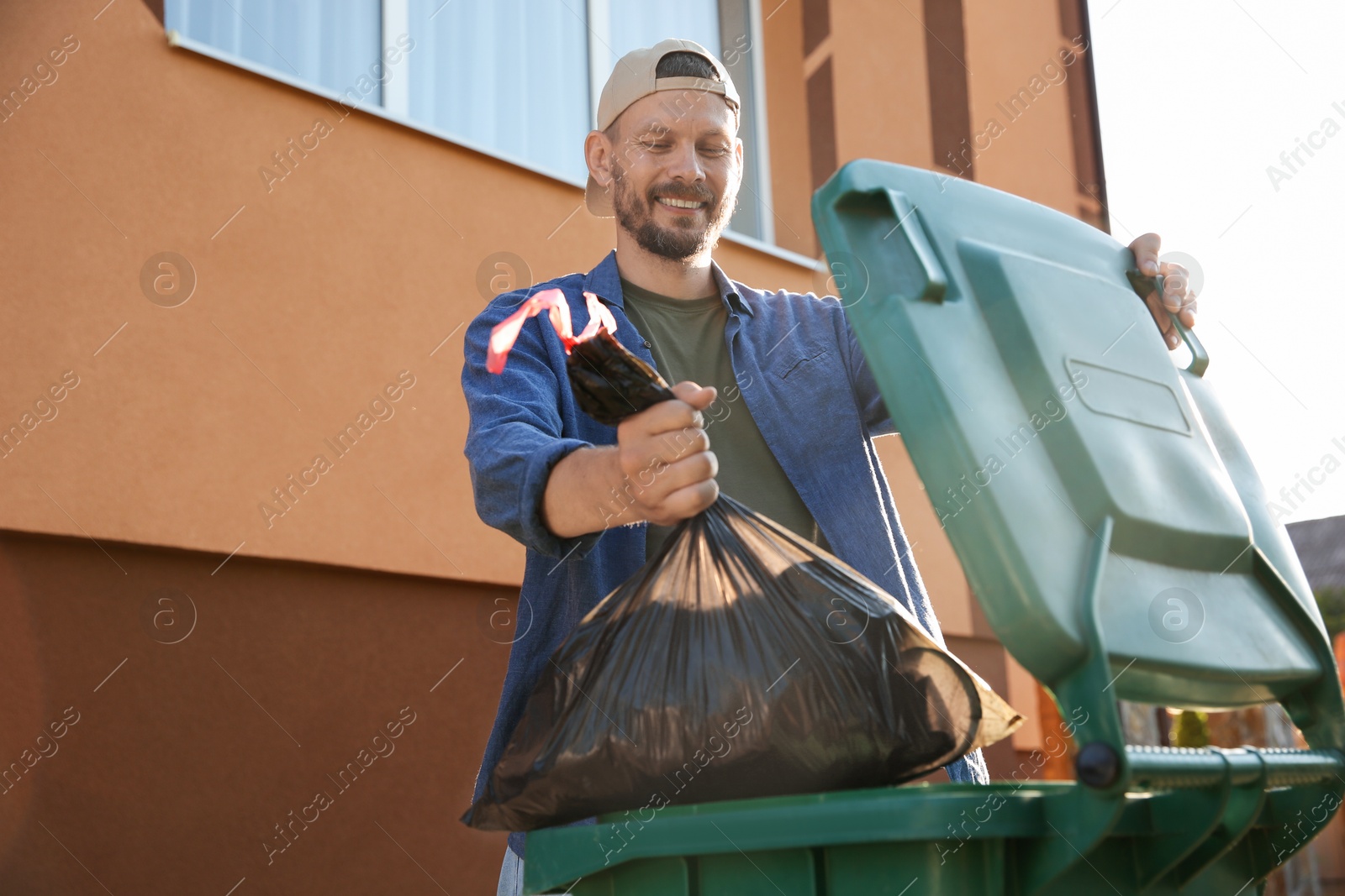 Photo of Man throwing trash bag full of garbage into bin outdoors, space for text