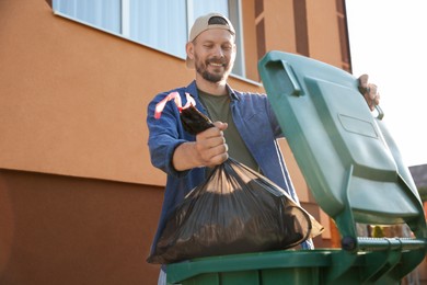 Man throwing trash bag full of garbage into bin outdoors, space for text