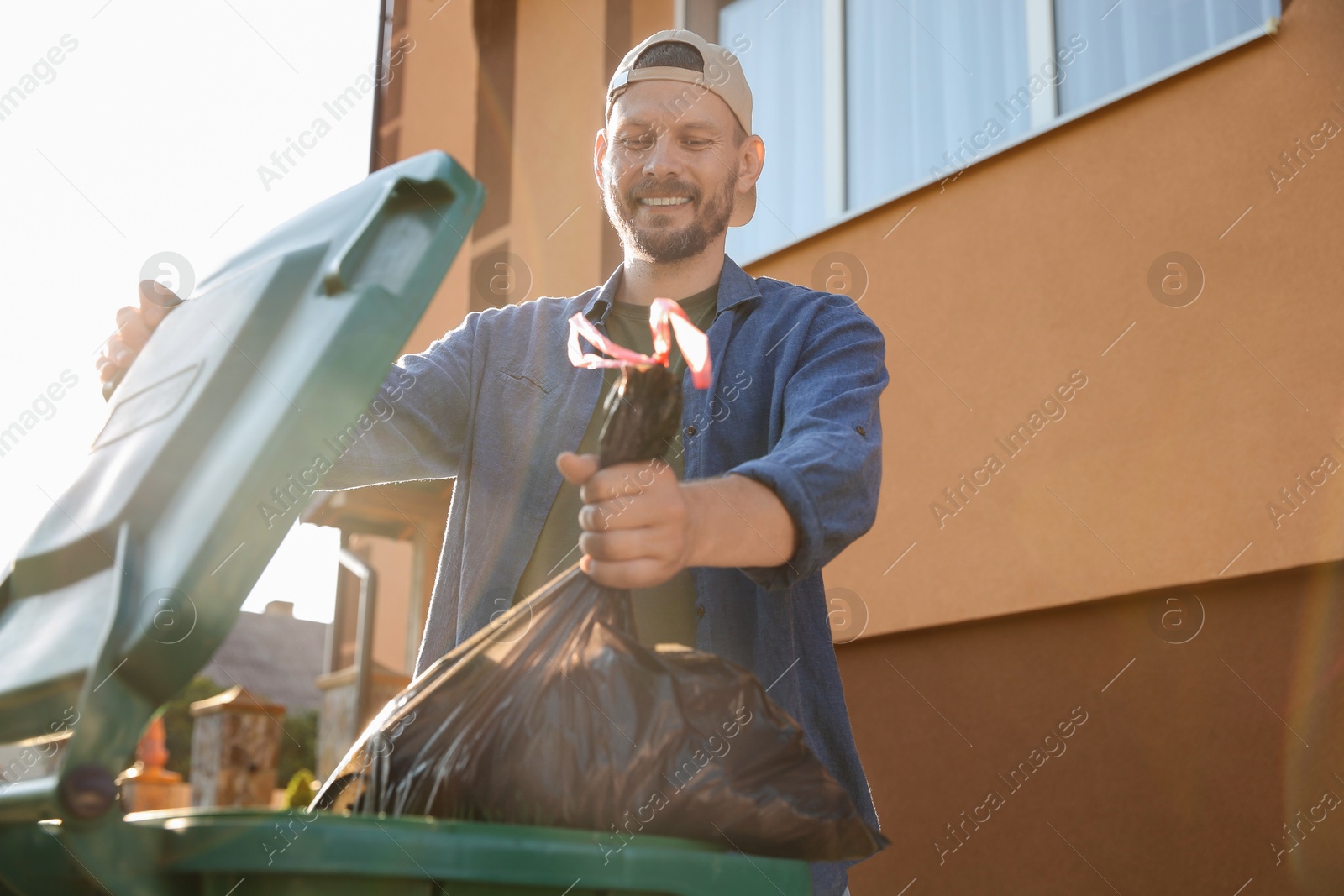 Photo of Man throwing trash bag full of garbage into bin outdoors, space for text