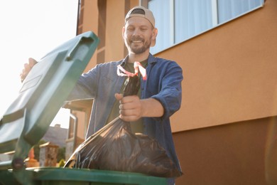 Man throwing trash bag full of garbage into bin outdoors, space for text